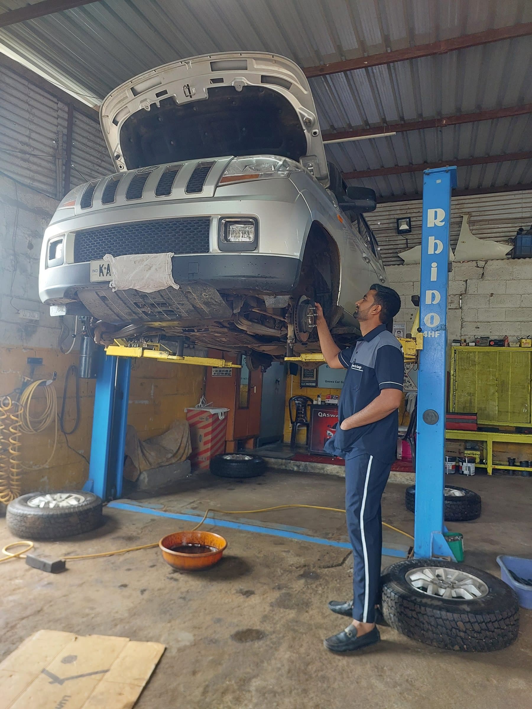 Mechanic inspecting a silver SUV on a blue hydraulic lift